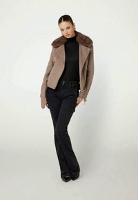 Brown wool blend jacket with faux fur collar, black fitted turtleneck, and dark, slim-fit cargo pants with visible pockets and seams.
