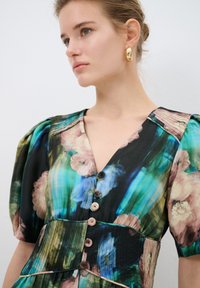 Blumengemustertes Kleid aus dunklem Stoff in Grüntönen, Blau und Pink. Mit gepufften Ärmeln und einer Knopfleiste.