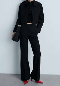 Veste noire courte avec poches à l'avant, associée à un pantalon noir évasé. Complété par des talons rouges à bout pointu et un sac à bandoulière noir.