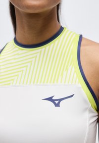 Κοντινό πλάνο ενός ατόμου που φοράει λευκό αθλητικό τοπ χωρίς μανίκια με νέον κίτρινα γεωμετρικά σχέδια και σκούρο μπλε λογότυπο στο στήθος.