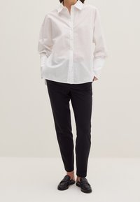 Bílá košile s límečkem, volného střihu a dlouhými rukávy. V kombinaci s černými slim-fit kalhotami a černými mokasínami.