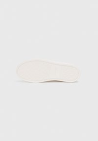 Suela de zapato de goma blanca con un patrón texturizado que presenta formas geométricas en relieve. "Calvin Klein" está grabado cerca del área del talón.