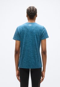 Μπλε αθλητική μπλούζα με ανάγλυ φη υφή, κοντά μανίκια, λαιμόκοψη και λεπτομέρεια λογότυπου στο πίσω μέρος; συνδυασμένη με μαύρο αθλητικό κολάν.