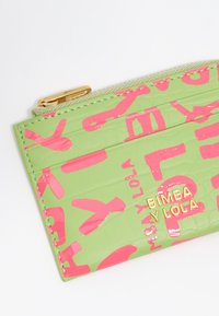 Zielona portmonetka z lakierowanej skóry, o fakturze krokodyla, z wyraźnym różowym napisem i złotym logo, z zamknięciem na zamek oraz kieszonkami na karty.