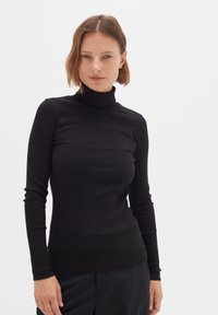 Schwarzes, geripptes Langarm-Turtleneck-Oberteil, enganliegendes Design, weiche Textur, mit hohem Kragen und dezenten Nähten, kombiniert mit schwarzen Hosen.