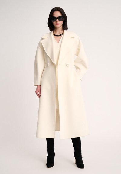 White wool coat with a wide lapel, double buttons, and straight fit. Paired with a beige dress and black knee-high stiletto boots.
