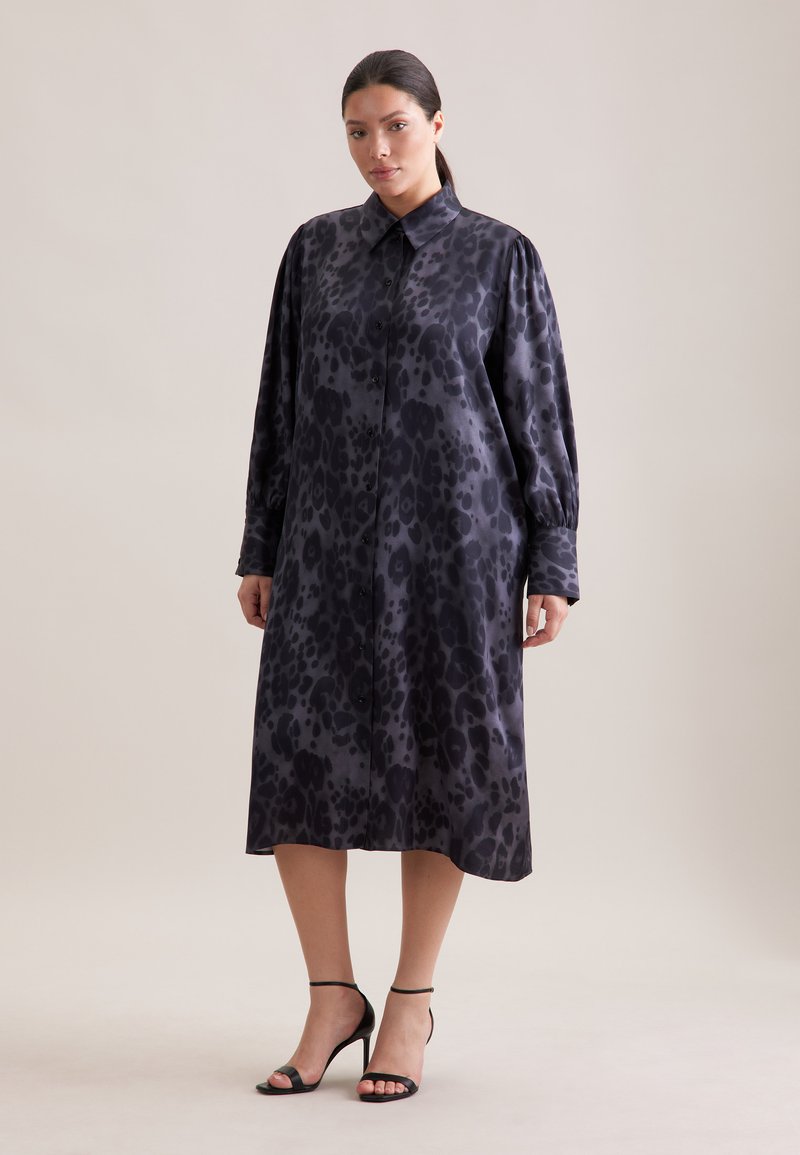 Lungo vestito nero con stampa leopardata, dotato di colletto, chiusura a bottoni davanti e maniche lunghe. Tessuto morbido e vestibilità comoda. Tacchi neri aperti.