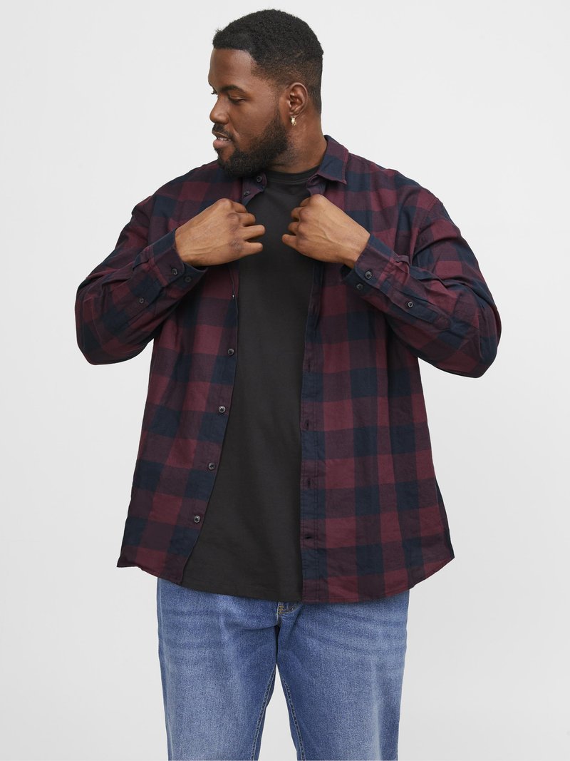 Rood en zwart geruite blouse met lange mouwen, knoopsluiting aan de voorkant en een ontspannen pasvorm. Gedragen over een zwart T-shirt, gecombineerd met een blauwe jeans.
