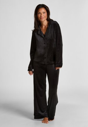 Ensemble de pyjama noir en tissu doux et texturé, comprenant une chemise à boutons avec col et un pantalon ample, présenté sur un mannequin.