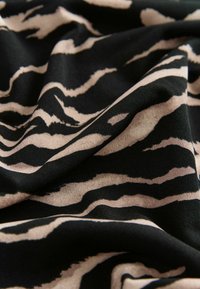 Tejido negro con un patrón de rayas de tigre onduladas en beige. La textura parece suave y blanda, con pliegues que resaltan el diseño.