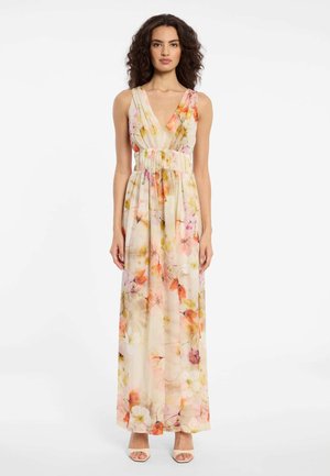 Frau trägt ein ärmelloses, bodenlanges Blumenkleid mit tiefem V-Ausschnitt und breitem Taillenbund, steht vor weißem Hintergrund.