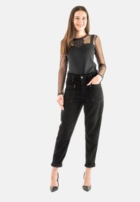 Pantalones de pana negra de cintura alta con puños doblados, combinados con una blusa negra con mangas largas de lunares transparentes y escote en forma de ondas.