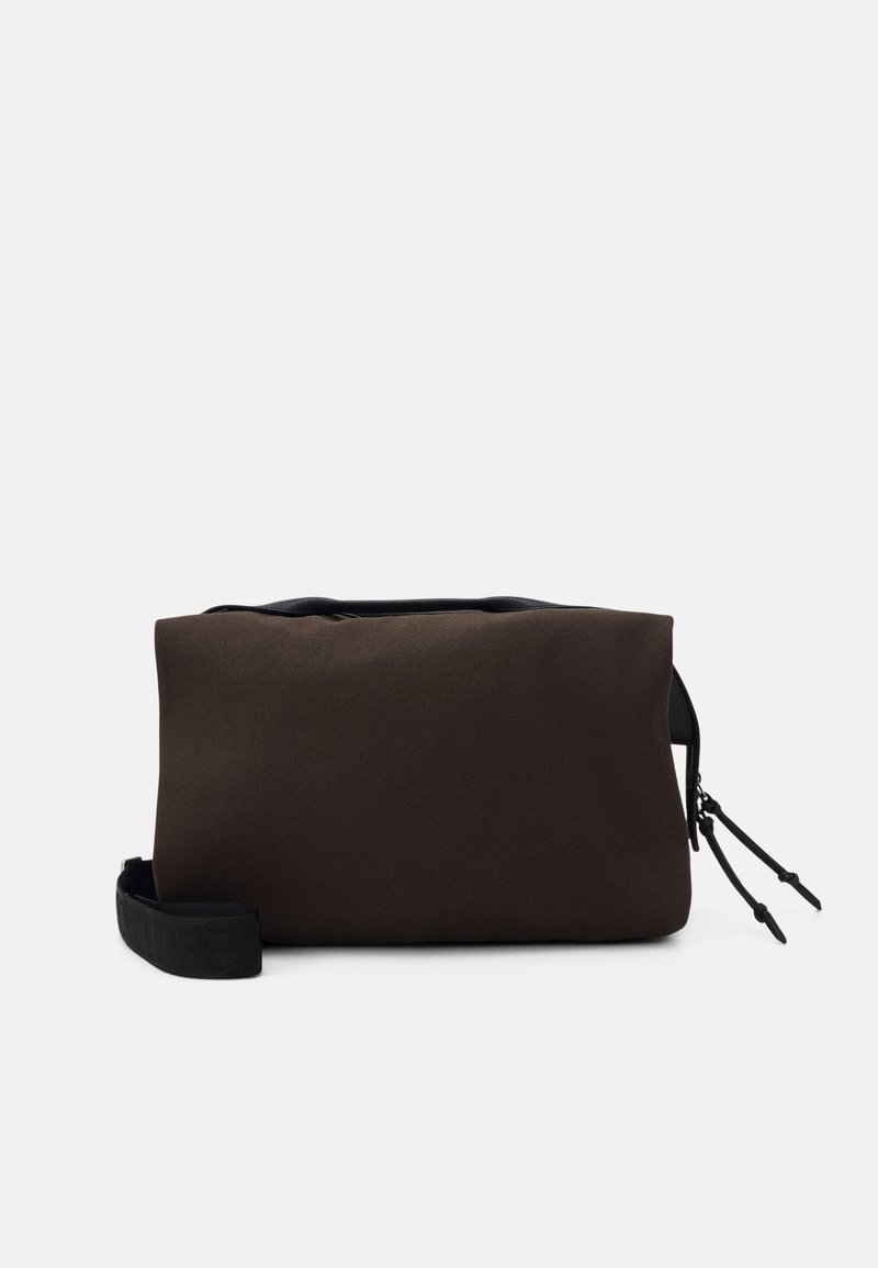 Petite pochette rectangulaire en tissu brun foncé avec fermeture éclair noire et bracelet de poignet noir réglable sur fond blanc.