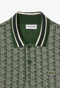 Zelené polo tričko s geometrickým vzorem, žebrovaným límečkem ve tmavě zelené barvě a bílými pruhy, se dvěma knoflíky a vyšívaným logo krokodýla na hrudi.