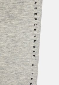 Light gray sweatpants made from cotton blend fabric, featuring vertical black text "ABERCROMBIE" along the side. Smooth texture, casual design.