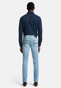 Camicia a maniche lunghe blu marina abbinata a jeans azzurri chiari con tasche posteriori ricamate. Vestibilità slim con polsini a bottoni e una texture liscia.