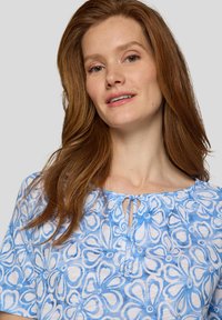 Bluse mit blauem Blumenmuster, runder Ausschnitt, Kordelzugdetail, kurzen Ärmeln und leichter Stofftextur.