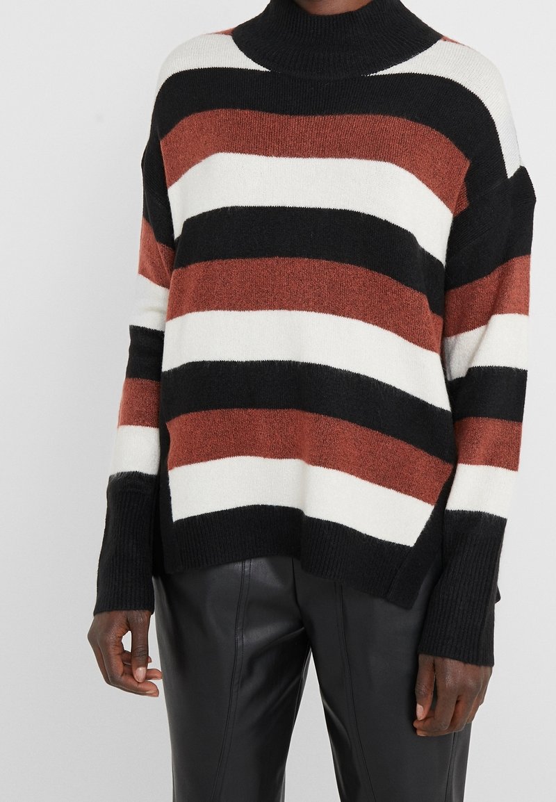 Pruhovaný svetr v černé, bílé a rezavé barvě, vyrobený z měkkého, texturovaného materiálu. Vysoký límec a volný střih s bočními rozparky.
