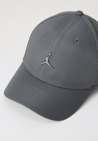 Grå baseballkasket lavet af tekstureret stof, med et hævet sort Jumpman-logo foran og ventilationshuller på toppen.