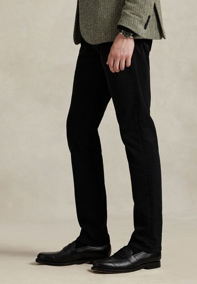 Svarte bomullsbukser med smal passform, kombinert med svarte loafers. En teksturert, hundetannsmønstret blazer er lagt over.