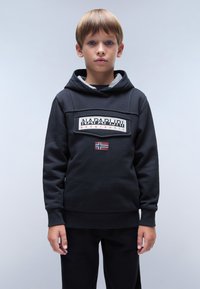 Felpa nera realizzata in cotone misto, con un logo patch frontale, foderata in grigio e un piccolo dettaglio con la bandiera norvegese. Indossata con pantaloni neri.