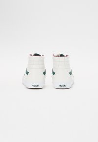 Valkoiset korkeakouluraket sneakersit, joissa on vihreät sivuviivat, pehmustetut varret ja vaaleanpunainen vuori. Varustettu kumipohjilla ja "Vans Off The Wall" -logolla kantapäässä.