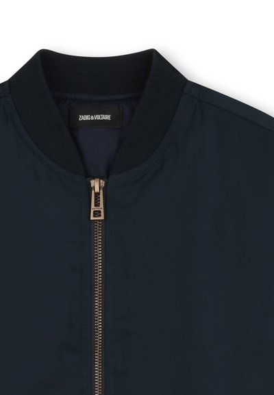 Veste bomber bleu marine avec col côtelé, fermeture éclair en métal doré et texture de tissu lisse. L'étiquette indique "Zadig & Voltaire".