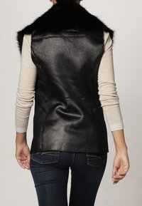 Schwarze Kunstlederweste mit hohem Kragen, ausgestattet mit einem Kunstfellbesatz, strukturiertem Material, figurbetontem Design und sichtbaren Nähten auf der Rückseite.
