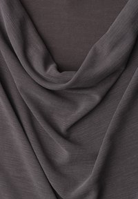 Tissu gris foncé avec une texture lisse et légère, drapé en plis doux sur une surface plane.