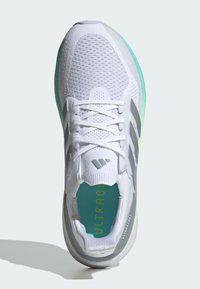 Biały but sportowy z siateczkową cholewką, zielonymi akcentami, szarymi paskami i niebieską wkładką z napisem "ULTRABOOST". Płaskie sznurowadła i wyściełany kołnierz.