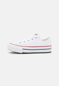 Zapatilla de lona blanca con suela de goma a rayas rojas y marinas, diseño de cordones y puntera reforzada. Presenta ojales metálicos y una puntera texturizada.