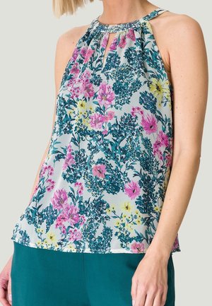 Woman wearing sleeveless halter neck top with pink, yellow, and green floral pattern, paired with teal pants.