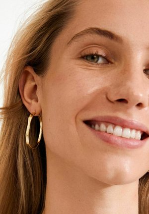 Gold hoop earrings with a textured, slightly twisted design. The earrings dangle and are visible against a light background.