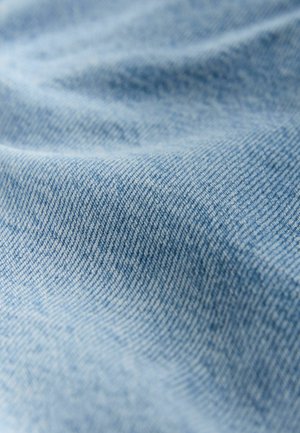 Material de denim albastru deschis cu o textură moale; model vizibil de os de pește și ondulații ușoare, evidențiind calitatea sa flexibilă.