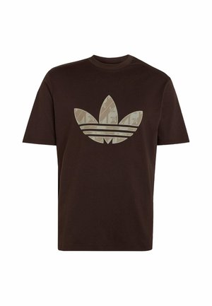 Camiseta de manga corta de color marrón oscuro con un gran logo trefoil beige de Adidas que presenta un sutil patrón de hojas en la parte delantera.