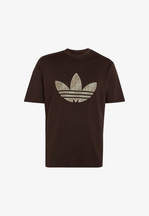 Camiseta de manga corta de color marrón oscuro con un gran logo trefoil beige de Adidas que presenta un sutil patrón de hojas en la parte delantera.