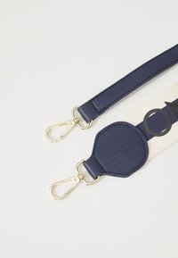 Bracelet en cuir bleu marine avec quincaillerie dorée, présentant une surface texturée et une section en toile avec des lettres noires, conçu pour l'attachement.