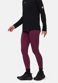Bordeaux leggings med en åtsittande design och sidfickor, kombinerat med en svart långärmad topp med en logotyp på bröstet och ärmen.
