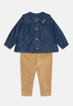 Camisa de mezclilla con un gran cuello, frente abotonado y bordado verde; combinada con pantalones de pana marrón claro y suave con textura acanalada.