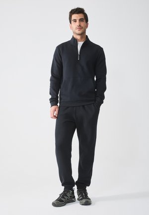 Black zip-up sweatshirt with a front pocket, paired with matching jogger pants and black athletic shoes, all made of soft, textured fabric.