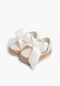 Witte canvas espadrilles met een gevlochten jute zool, voorzien van grote satijnen strikken aan de voorkant en een ronde vorm. Zachte textuur.