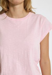 Šviesiai rožinė marškinėliai su minkšta, tekstūruota medžiaga, apvaliu kaklu ir trumpomis rankovėmis, su laisvu siluetu ir minimaliais siūlėmis.