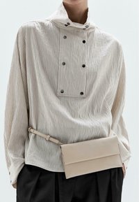 Camicia a maniche lunghe a righe verticali di un beige chiaro, con colletto alto e dettagli con bottoni. Abbinata a una borsa a tracolla liscia e piatta beige.
