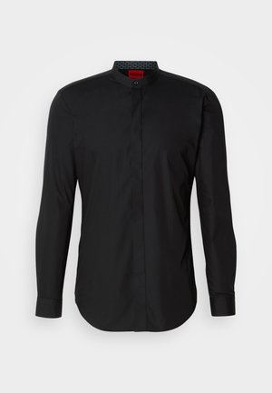 Chemise noire à manches longues avec col mandarin, fabriquée en tissu lisse, dotée d'une fermeture à boutons sur le devant et d'un ourlet arrondi.