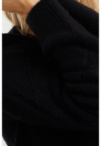 Černý pletený svetr s texturovanou látkou, širokými rukávy a pohodlným, volným střihem, s viditelnými detaily příze a měkkým povrchem.