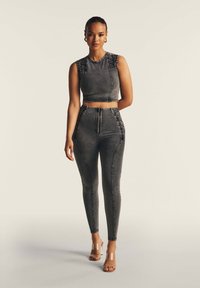 Cropped top in denim grigio scuro con dettagli testurizzati sulle spalle, abbinato a leggings a vita alta coordinati con cuciture laterali intricate.