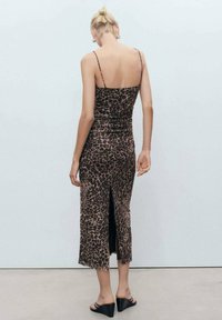 Smeđa haljina midi dužine s leopard uzorkom, tankih naramenica, prilagođenog dizajna, sa bočnim prorezom i glatkom teksturom. Uparena s crnim sandalama na petu.