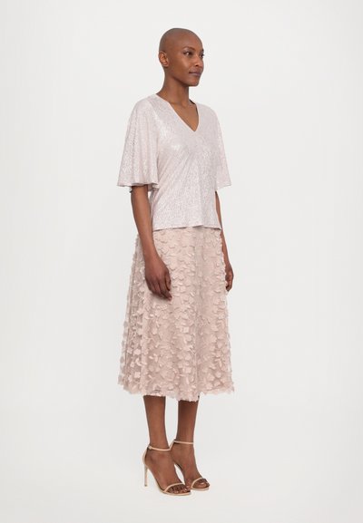 Pale pink sequin top with short flutter sleeves, paired with a knee-length lace skirt featuring floral appliqués and nude high-heeled sandals.
