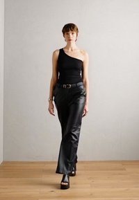 Černý top na jedno rameno v kombinaci s černými kalhotami z umělé kůže a robustními platformovými sandály; hladké textury a elegantní silueta.