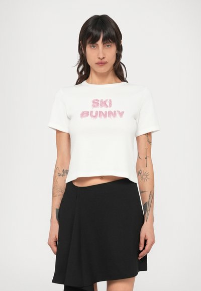 Λευκό cropped t-shirt με ροζ χνουδωτό κείμενο "SKI BUNNY." Κοντά μανίκια και στρογγυλή λαιμόκοψη. Συνδυασμένο με μαύρη φούστα.